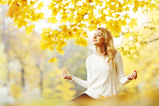 Beautiful young woman meditating outdoors in autumn park