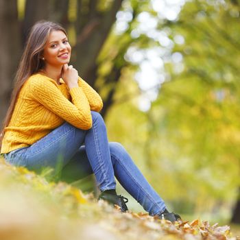 Beautiful woman sitting on autumn leaves in park