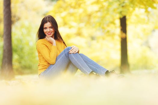 Beautiful woman sitting on autumn leaves in park