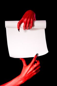 Red devil hands with paper scroll pointing at signature place, isolated on black background 