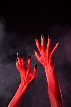 Red devil hands with black sharp nails, Halloween theme, studio shot over smoky background 
