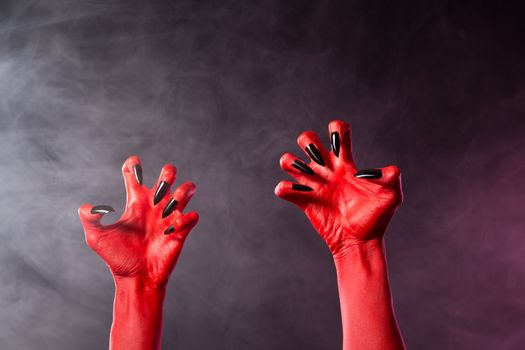 Spooky red devil hands with black glossy nails, Halloween theme, studio shot over smoky background 