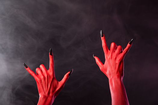 Red devil hands showing heavy metal gesture, studio shot on smoky background 