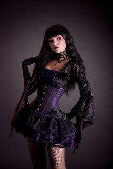 Romantic gothic girl in purple and black gothic Halloween outfit, studio shot on black background 