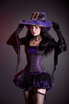 Smiling witch in purple and black gothic Halloween costume, studio shot on black background 