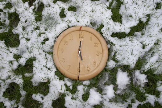 a broken clock face in the snow covered grass as if frozen in time and time has stopped