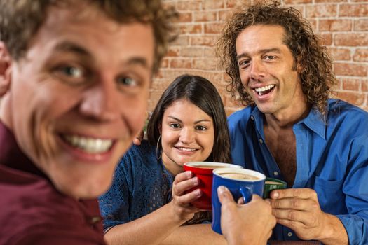 Excited friends toasting with coffee mugs in cafe