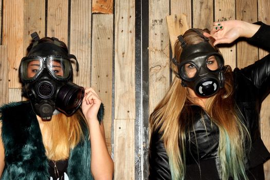 Two women in front of a wooden wall with gasmasks.