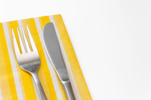 Stainless steel fork and knife on a yellow napkin.