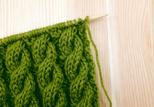 Green coiled rope cable knitting stitch on the needle, on a wooden background