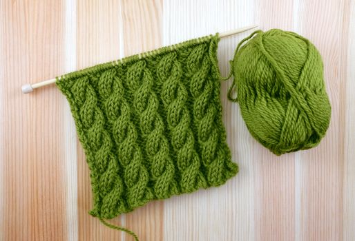 Rich green coiled rope cable stitch knitting with a ball of wool on woodgrain