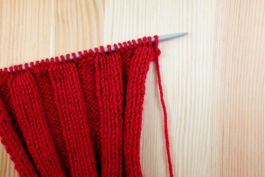Red knitting on the needle in rib stitch, on a wood background