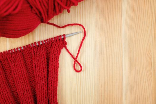 Red rib stitch on the knitting needle with a ball of wool, on wood