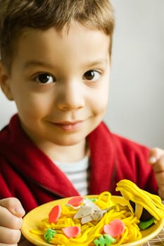 Portrait of cute child posing with his original spaghetti dish, made in colorful plasticine