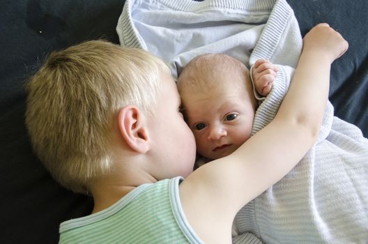 Baby with big eyes beeing cuddled by his older brother