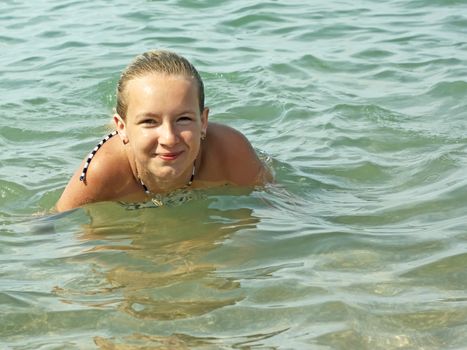 Smiling teenage girl swimming in sea water in warm sunny weather