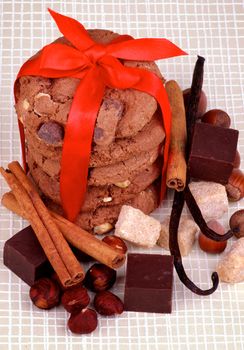 Stack of Delicious Christmas Cookies Tied with Red Ribbon and Chocolate Cubes, Nuts, Cinnamon Sticks and  Vanilla Pods closeup on Checkered background
