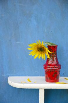 red vase with one sunflower blossom on white shelf