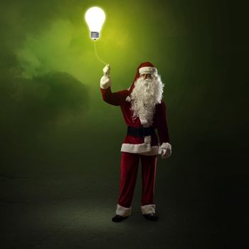 Santa Claus is holding a shining lamp on a string