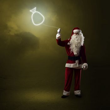 Santa Claus is holding a shining symbol of the bag with gifts on a string