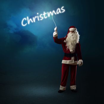 Santa Claus is holding a shining Christmas word sign on a string