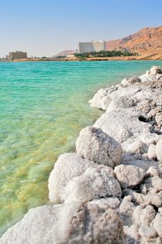 Vertical oriented image of salt formations on the shores of Dead Sea and touristic resorts on background in Israel.