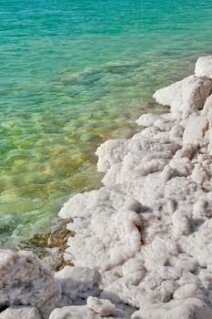 Vertical oriented image of salt formations on the Dead Sea along beautiful clear aquamarine colored water in Israel.