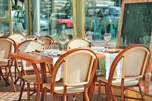 Tables, chairs and wine glasses on white napkins at outdoor restaurant in Menton, France.