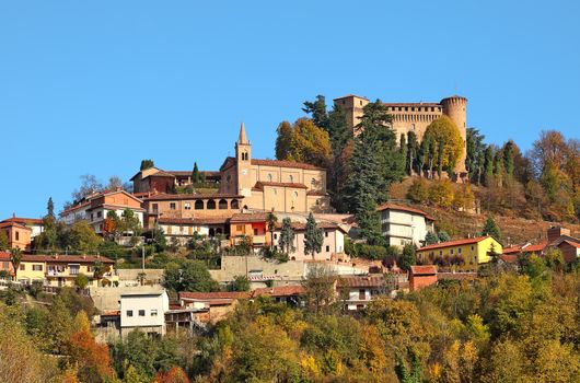 Small town and medieval castle among autumnal trees on top of the hill in Piedmont, Northern Italy.