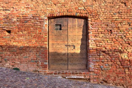 Red brick exterior wall of old house with wooden door on cobbled street in small italian town.