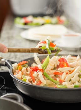 Closeup of female cooking vegetables and chicken for mexican food in a black pan