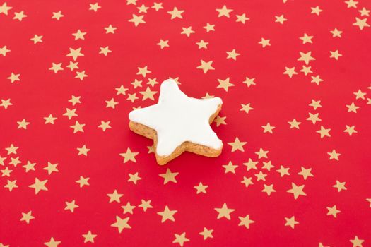 Star shaped cinnamon biscuit on red background with golden stars