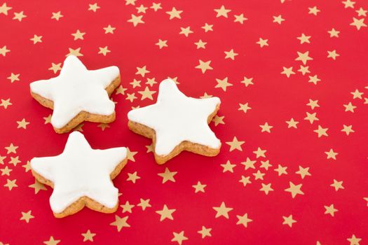 Star shaped cinnamon biscuits on red background with golden stars