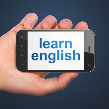 Education concept: hand holding smartphone with word Learn English on display. Generic mobile smart phone in hand on Dark Blue background.