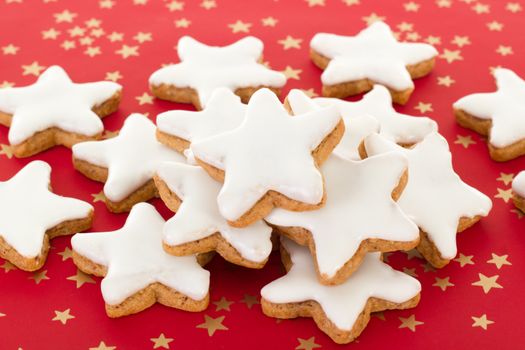 Star shaped cinnamon biscuits on red background with golden stars
