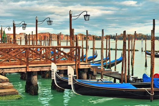 Gondolas moored in a row at wooden pier on Grand Canal in Venice, Italy.