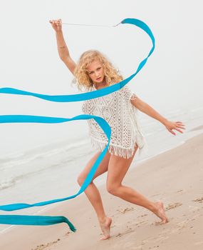Young beautiful gymnast woman dance with ribbon on the beach at foggy day
