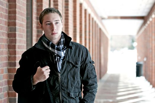 A portrait of a young man standing in an outdoor corridor with his backpack.