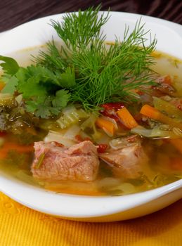 Tasty Homemade Vegetable Soup with Boiled Beef and Greens in White Bowl closeup  on Yellow Napkin