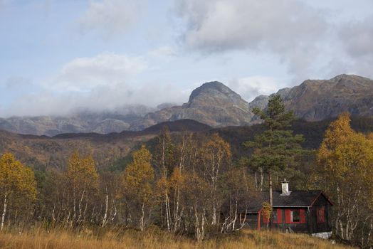 A small cabin surrounded by trees in autumn,  in a beautiful mountain landscape scenery