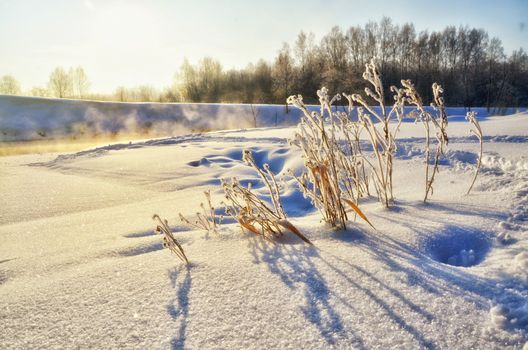 Winter landscape with sun and frozen river in sunset