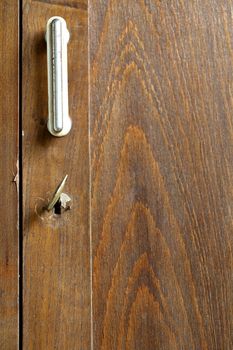 Metal handle and keyhole with a key of an old wooden wardrobe.
