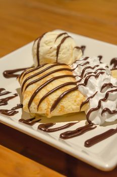 Crepes with banana , chocolate sauce  served with whipping cream and vanilla ice cream over white dish
