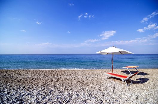 Recliner and umbrella on a pebble beach.