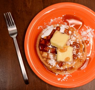 waffles with powdered sugar, butter and syrup on wood