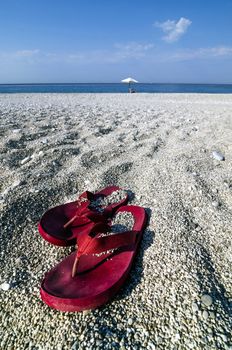Pair of flip-flops on a pebbly beach with umbrella in background.