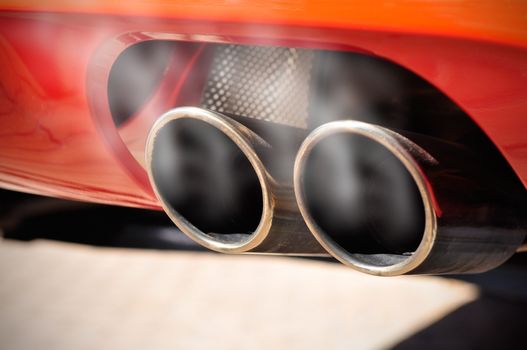 Close up of a red car dual exhaust pipe with smoke around it
