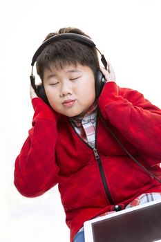 Vertical shot of a young Asian boy in red enjoying his moment  listening to music with a headphone isolated on white.