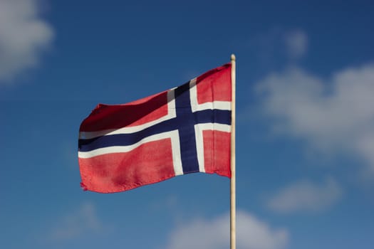 A Norwegian flag against a blue sky with white clouds.