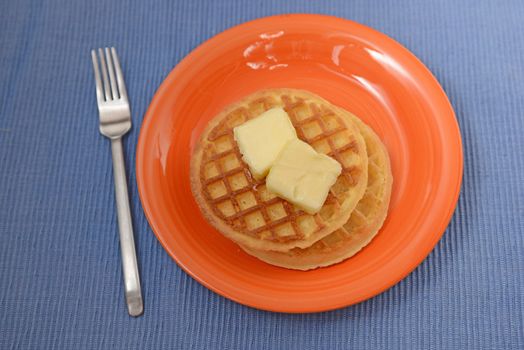 two waffles for breakfast on orange plate and bright blue background